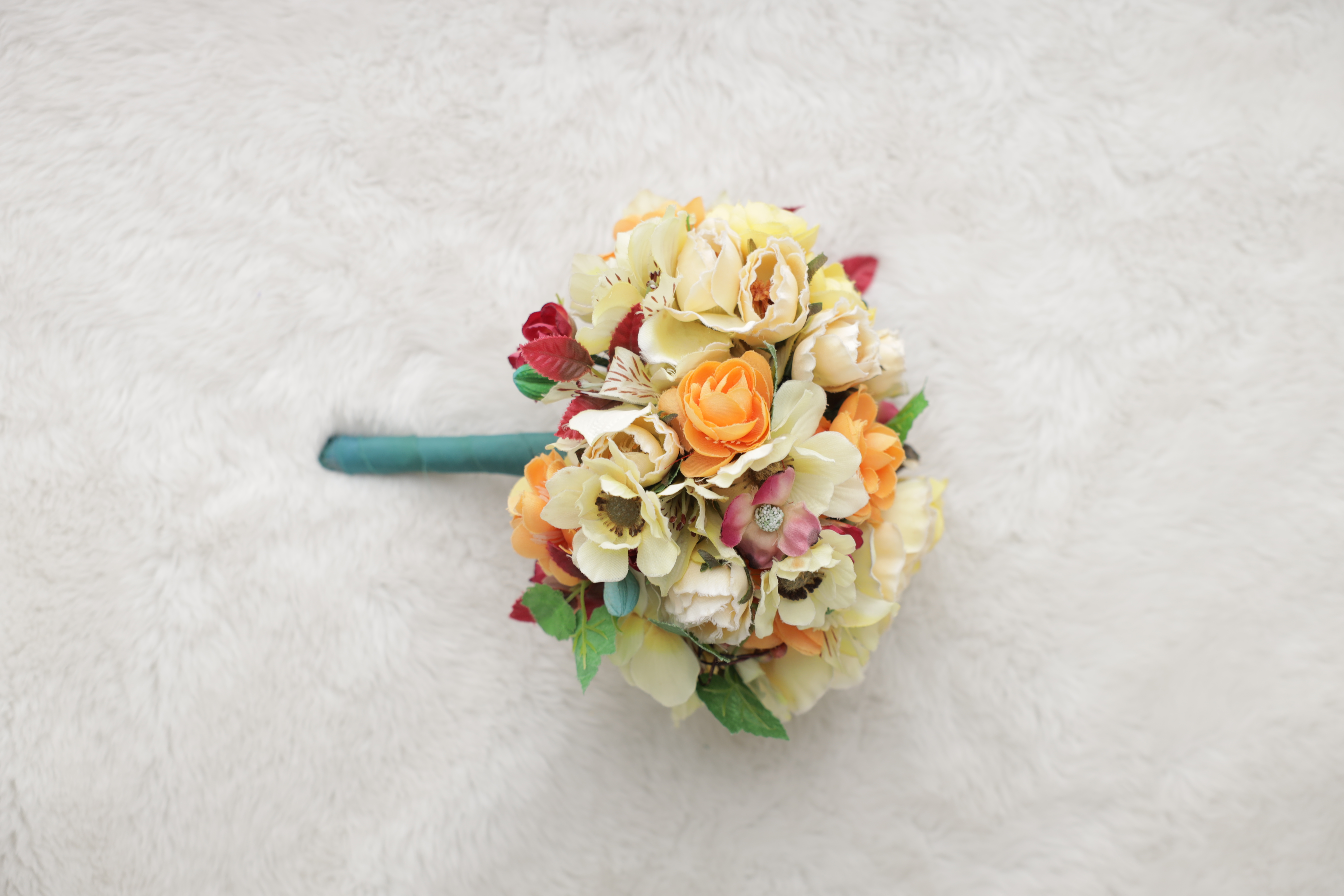 イエローとオレンジの花にターコイズのリボンを巻いた明るいブーケ