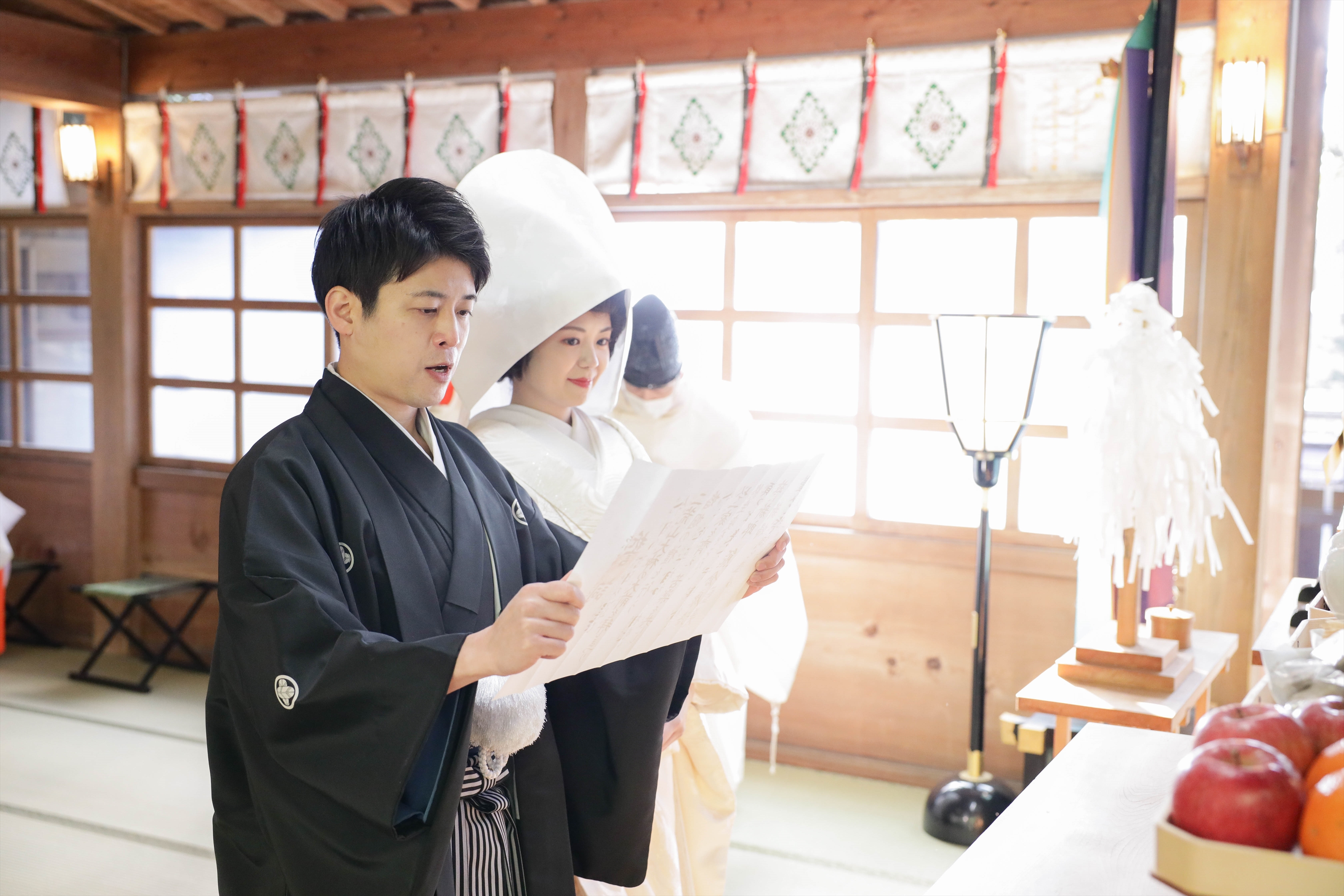 神前で誓詞を読み上げる黒紋付袴の新郎と綿帽子の白無垢姿の新婦