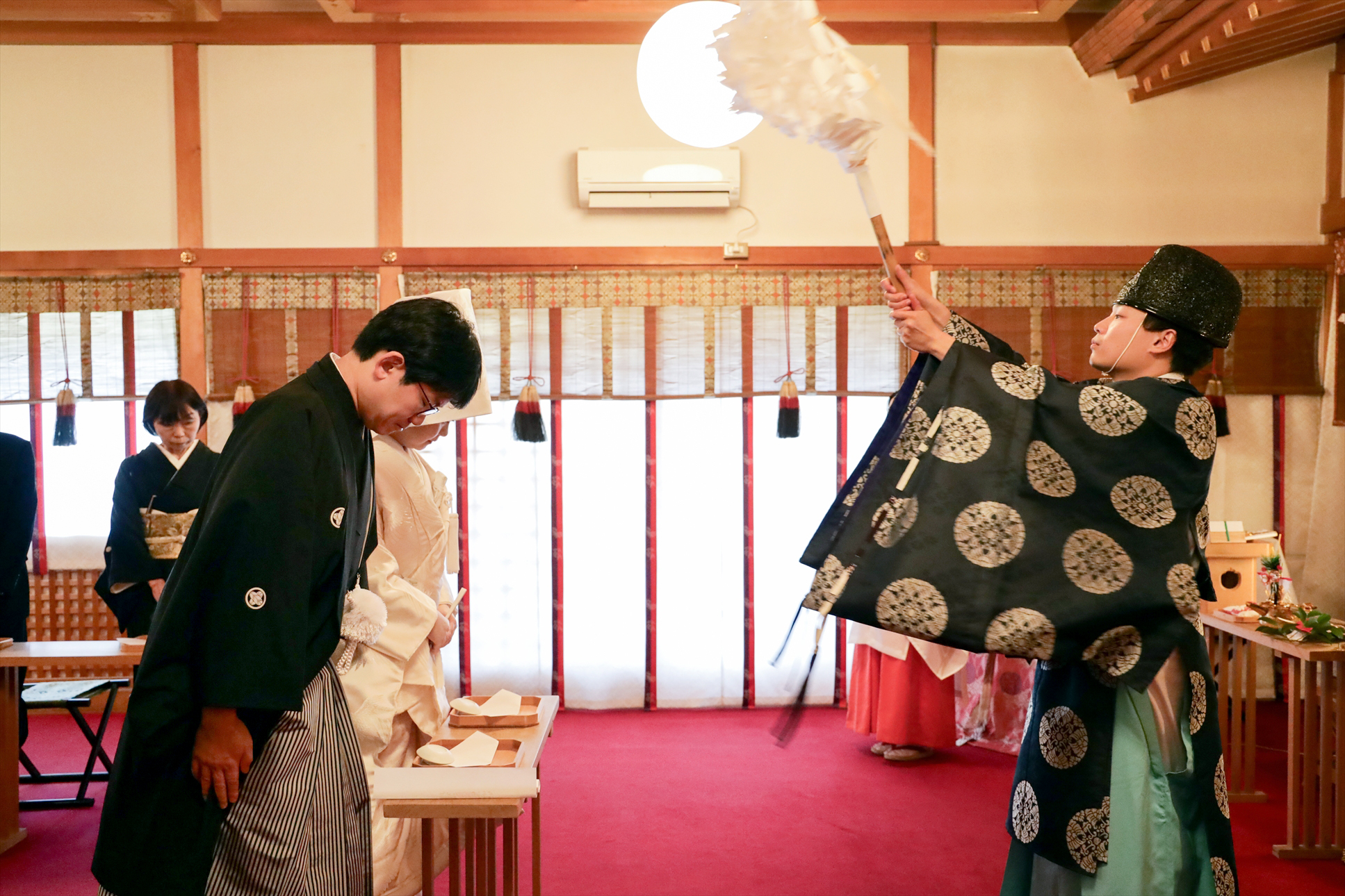 神職のお祓いを受けて頭を下げる黒紋付袴の新郎と白無垢の新婦