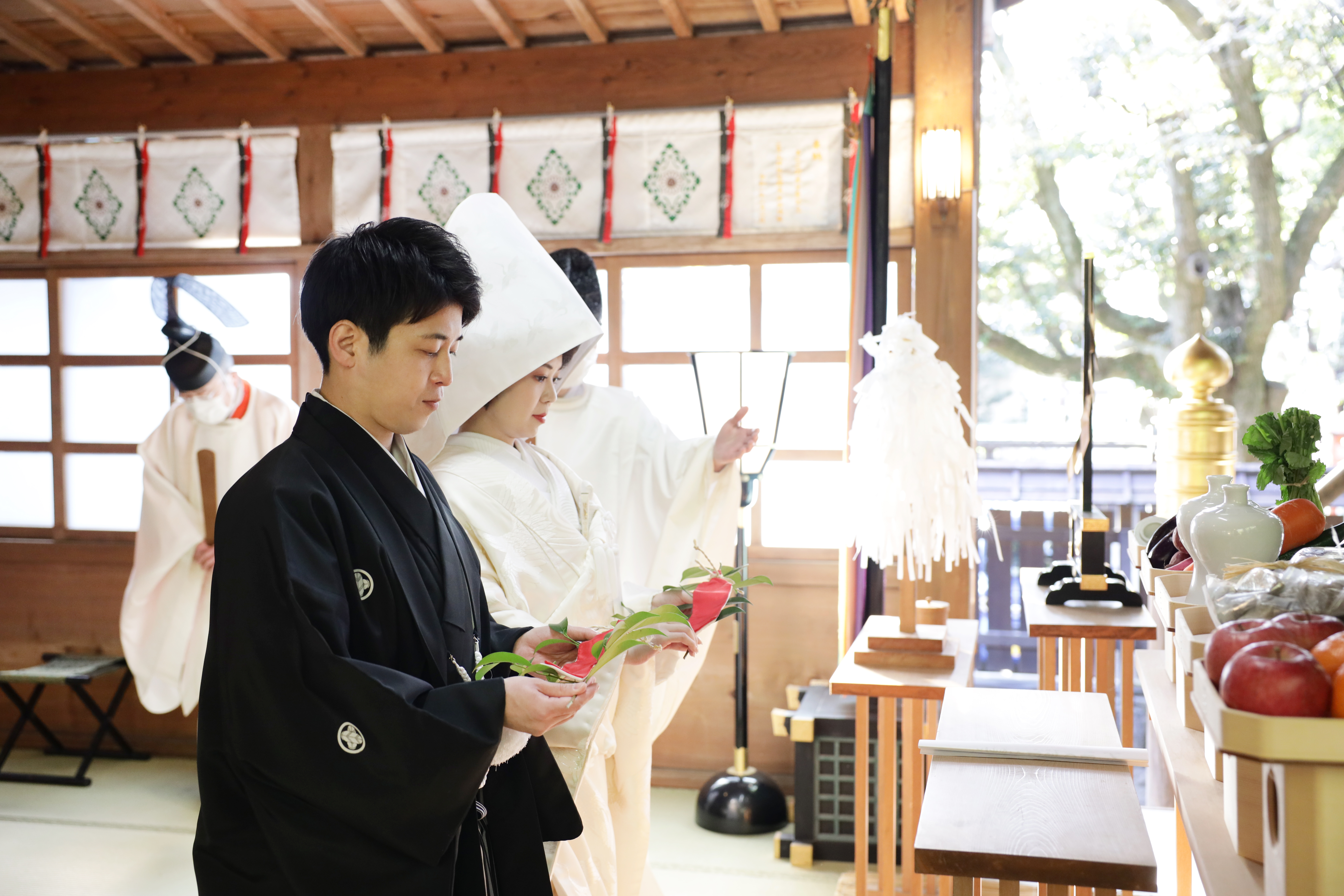 拝殿の神前式で神職に見守られ玉串を捧げる綿帽子に白無垢の花嫁と紋付袴の花婿