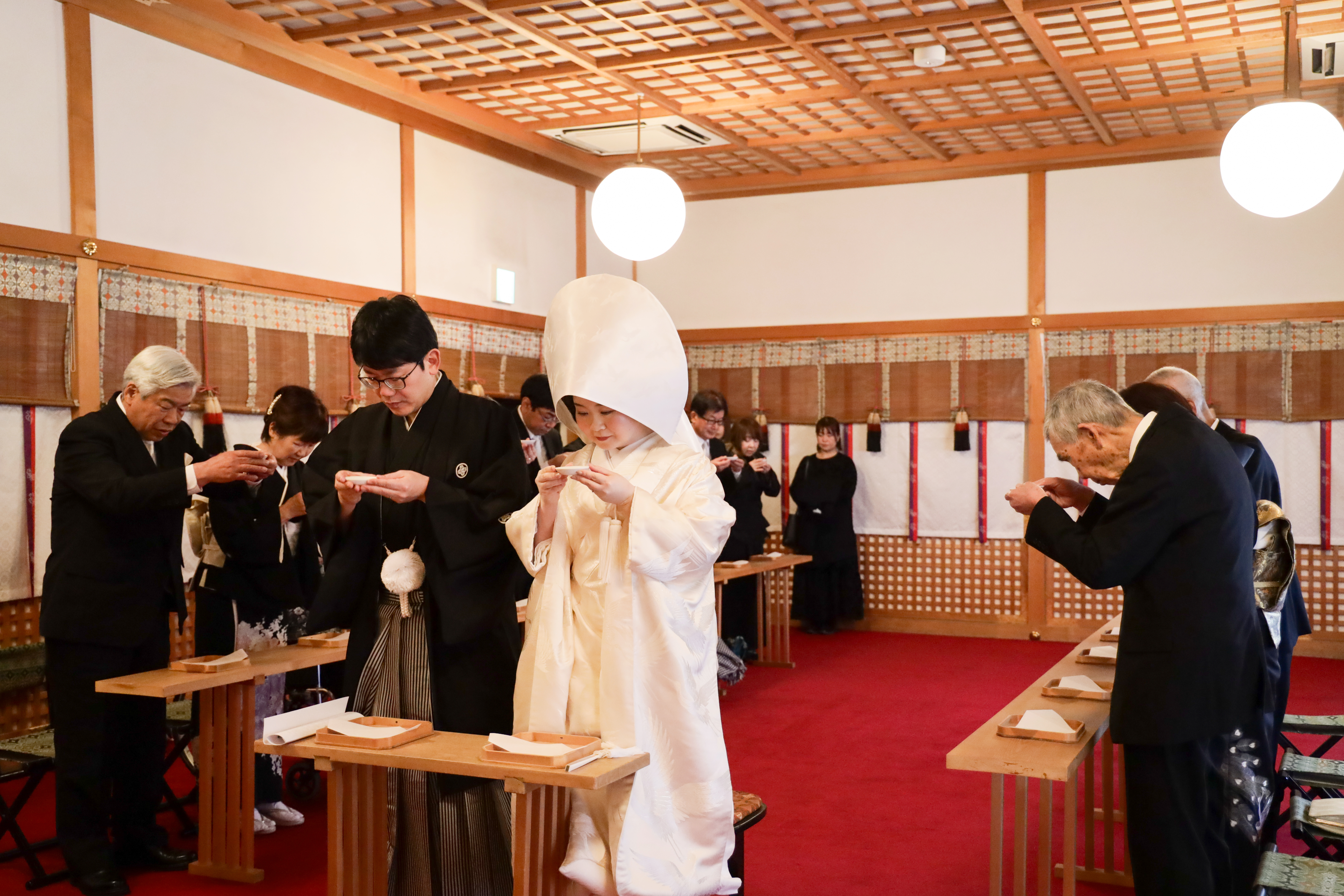 祭殿の神前式で親族とともに三三九度の盃を交わす綿帽子に白無垢の花嫁と紋付袴の花婿