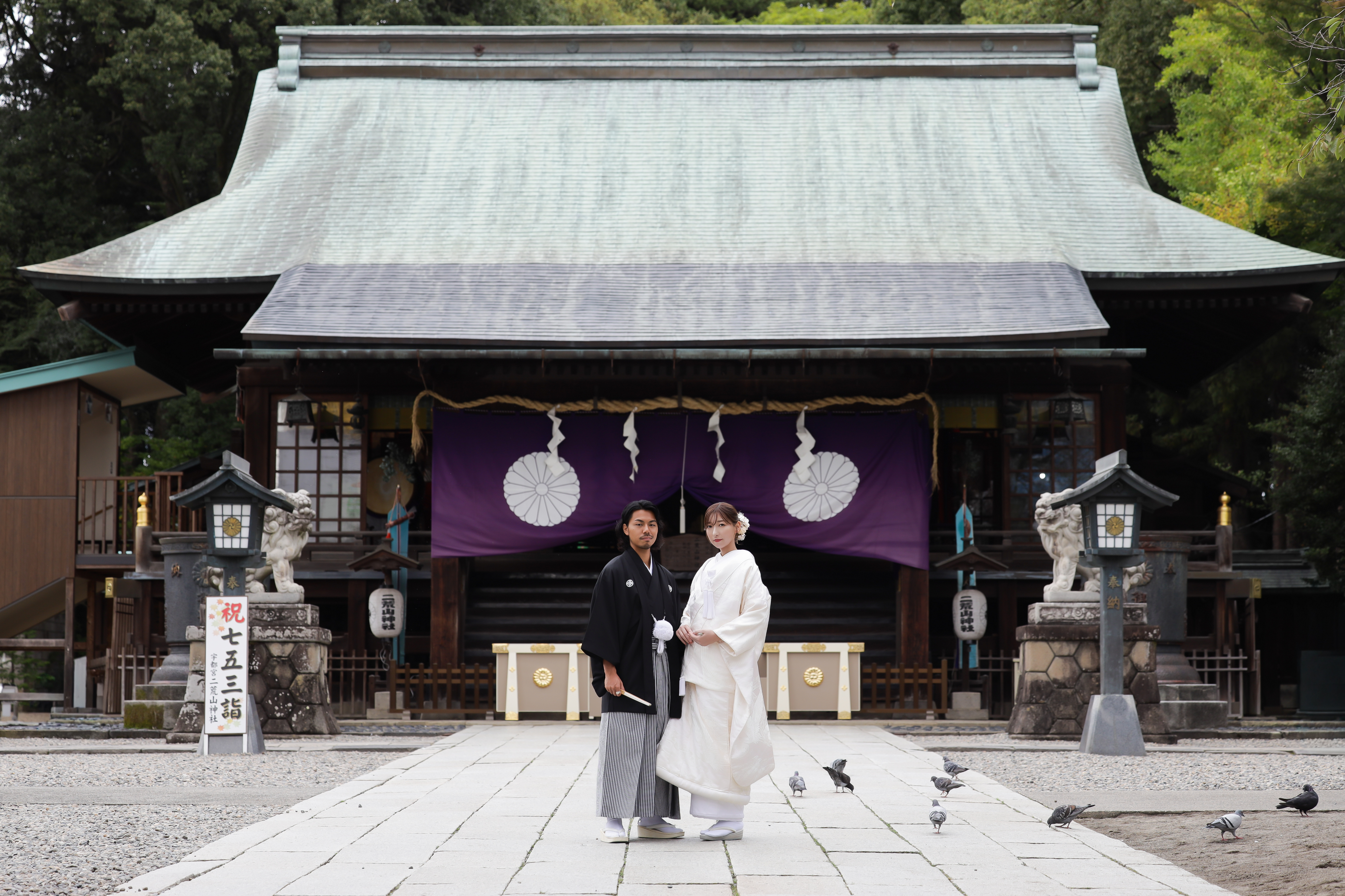 紫の幕が下がる二荒山神社拝殿の前に並んで立つ白無垢の新婦と紋付袴の新郎