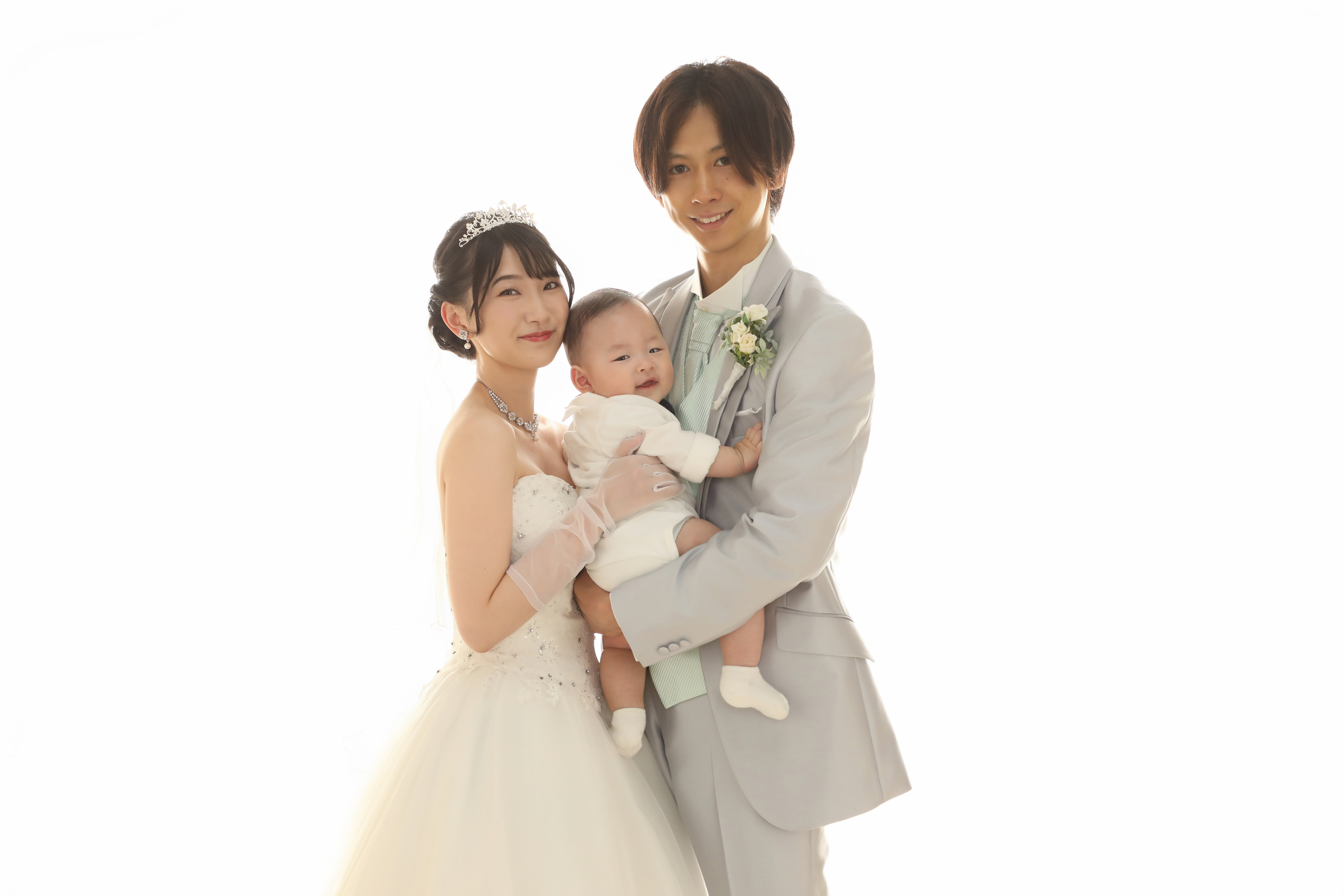 白ホリゾントで赤ちゃんを抱くウェディングドレスの新婦とグレータキシードの新郎