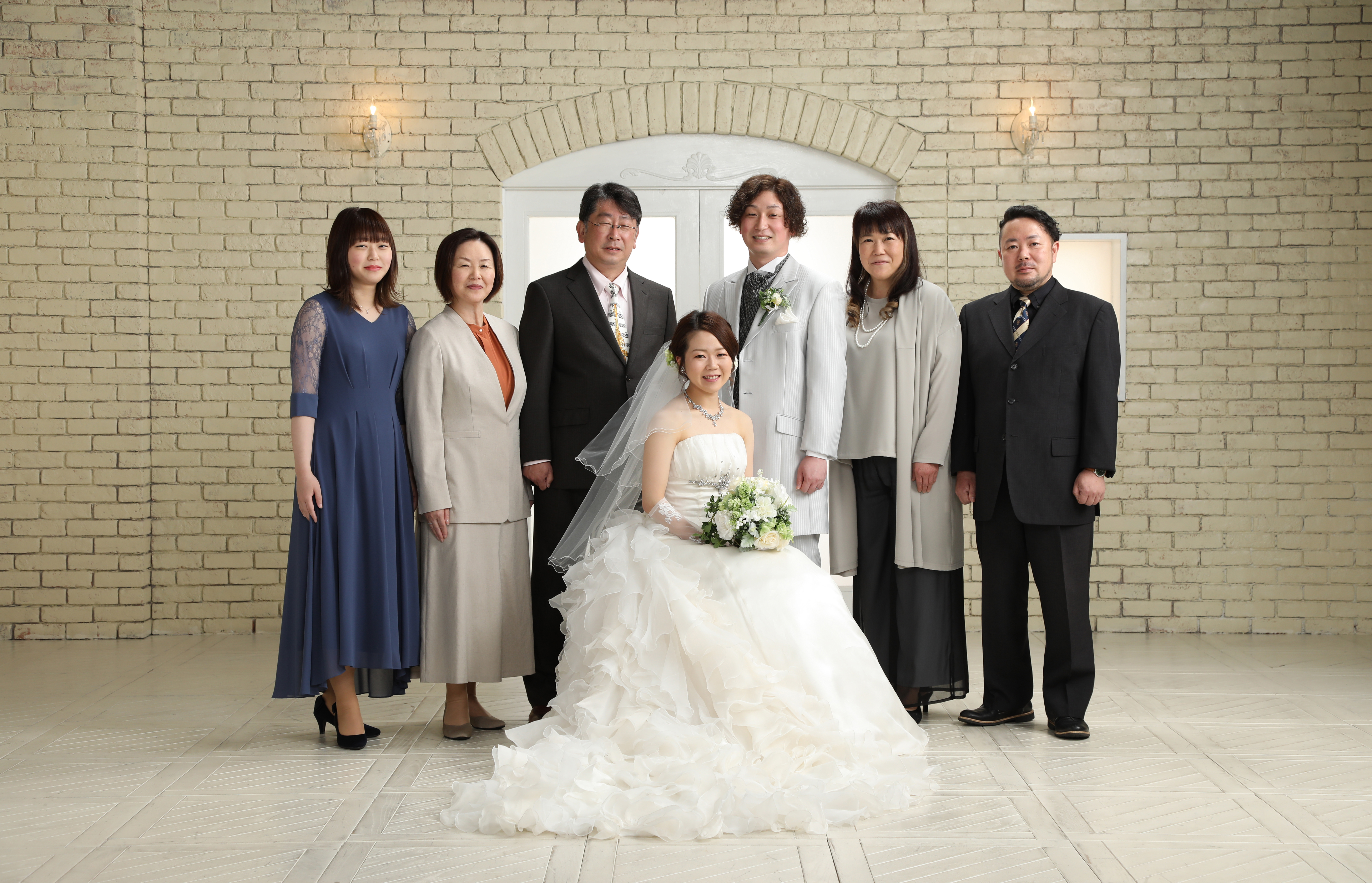 レンガ壁のスタジオでご家族7人と並ぶウェディングドレスの新婦と新郎