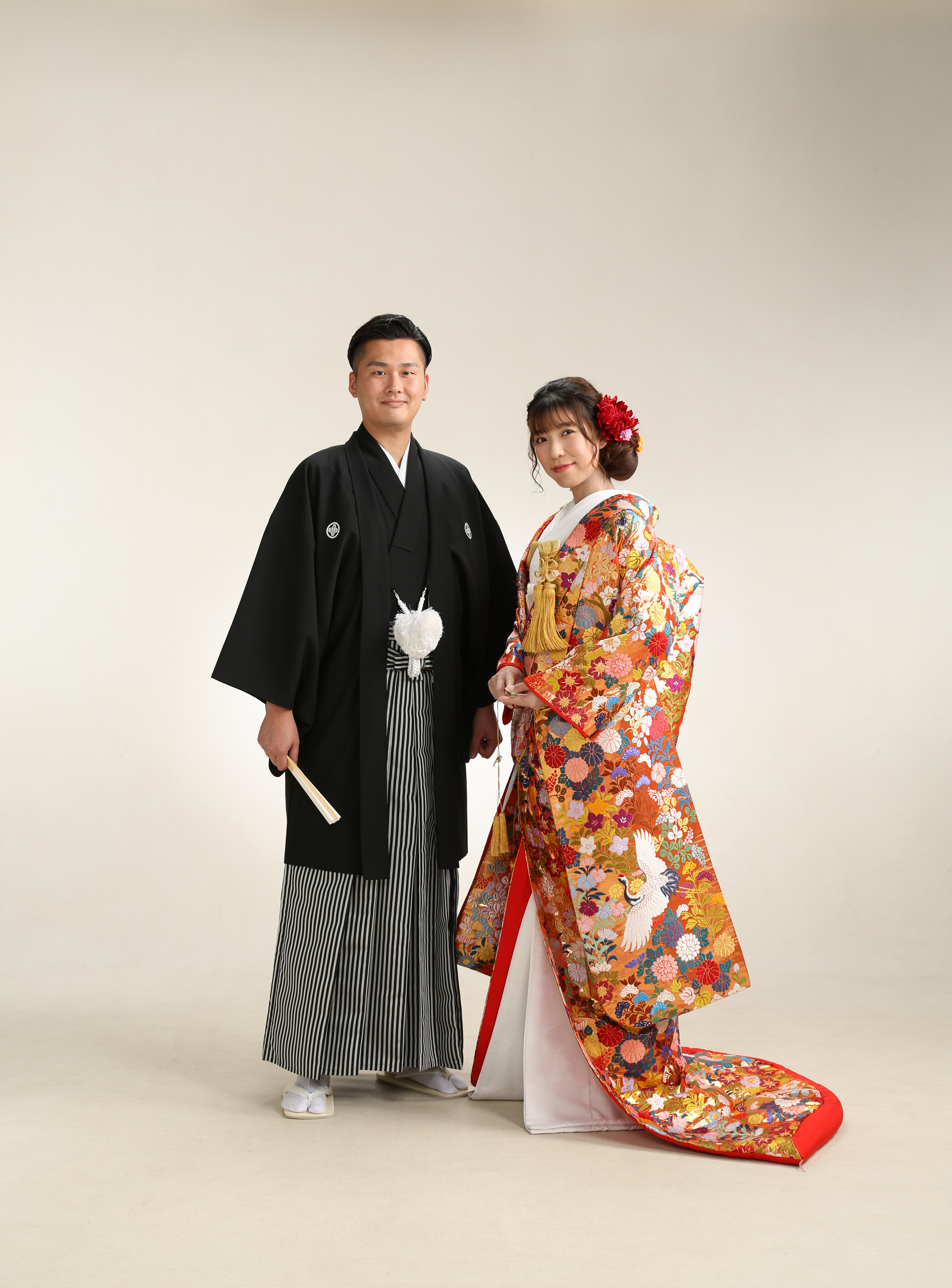 オレンジ地に花と鶴の色打掛をまとった新婦と黒紋付袴の新郎の全身