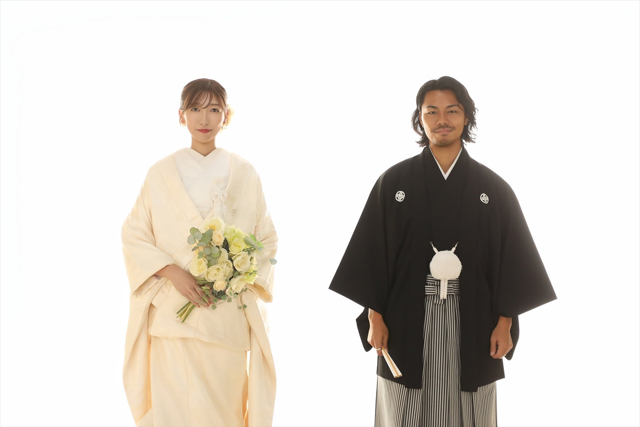白背景でバラのブーケを持つ白無垢の新婦と黒紋付袴の新郎が並ぶ