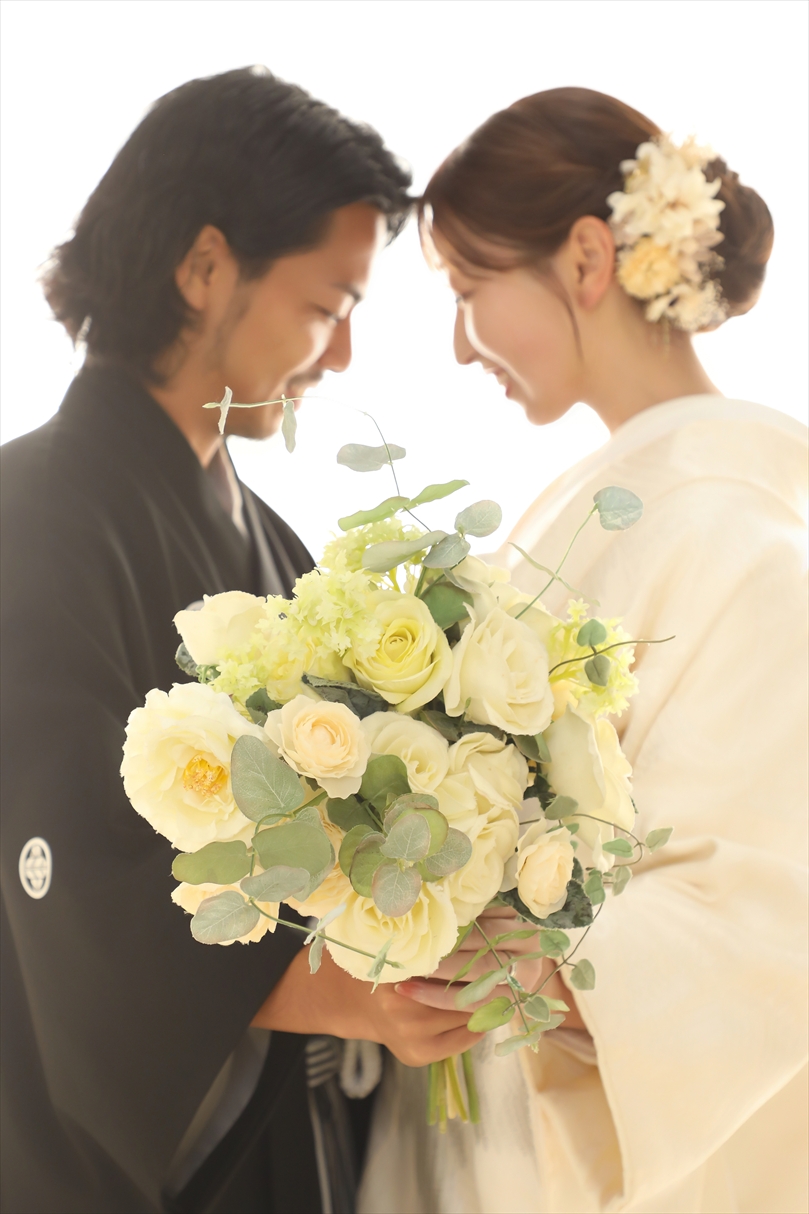 クリーム色のバラのブーケ越しに見つめ合う白無垢の新婦と黒紋付袴の新郎