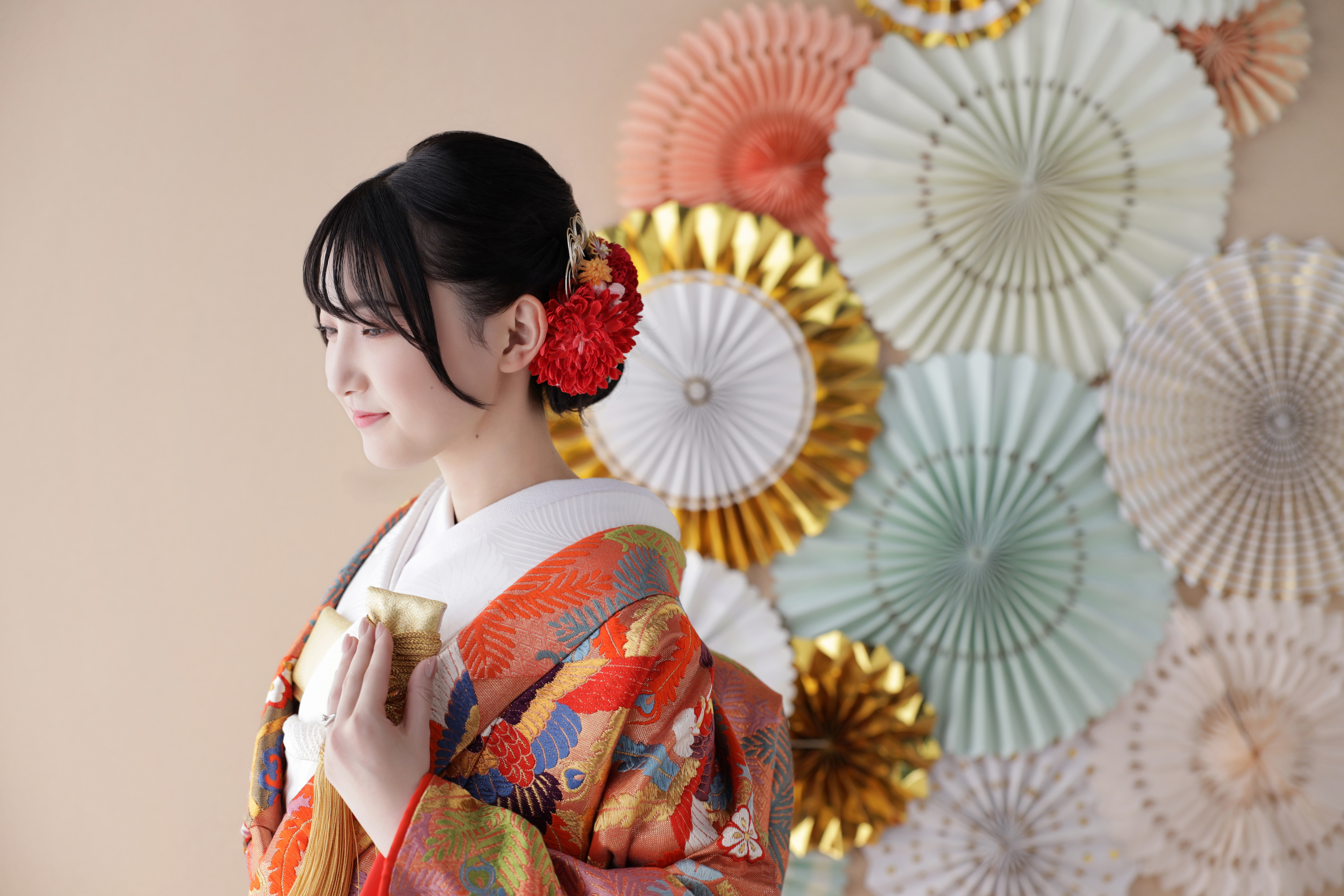 ペーパーファンの前で赤い花の髪飾りをつけ横顔を見せる色打掛の新婦