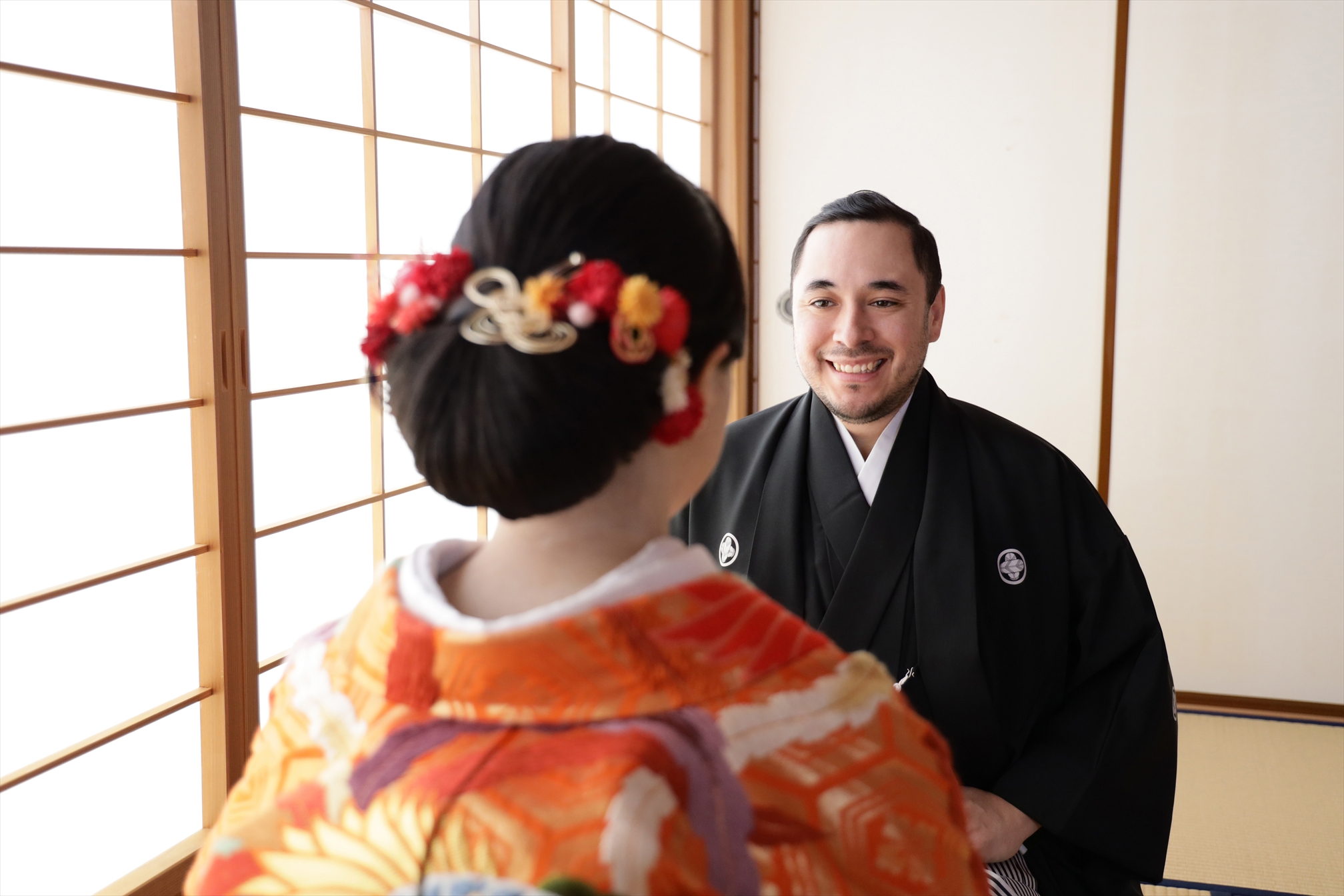 和室で色打掛の新婦を見つめて笑う黒紋付袴の新郎