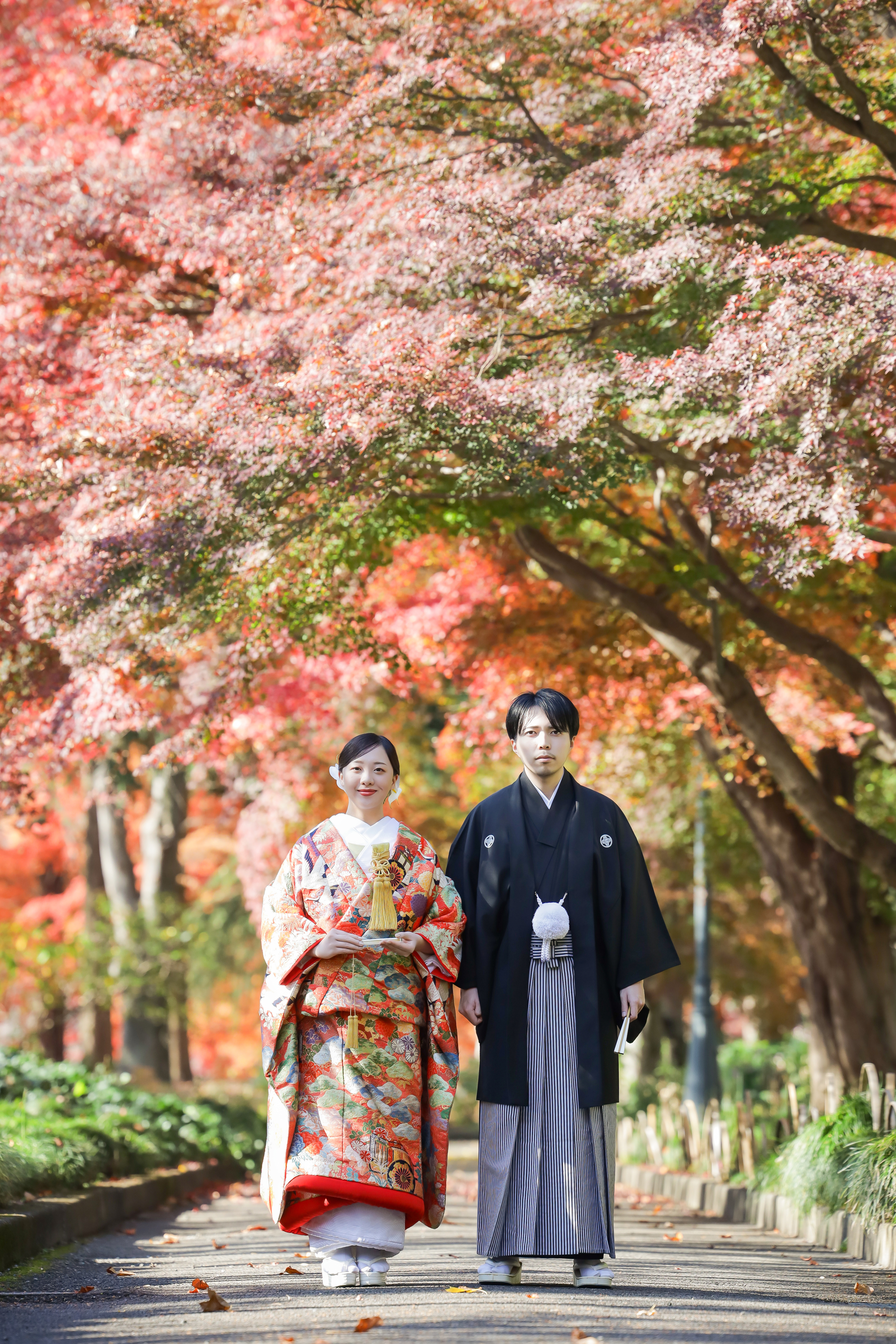紅葉のトンネルの下に並んで立つ色打掛の新婦と黒紋付袴の新郎