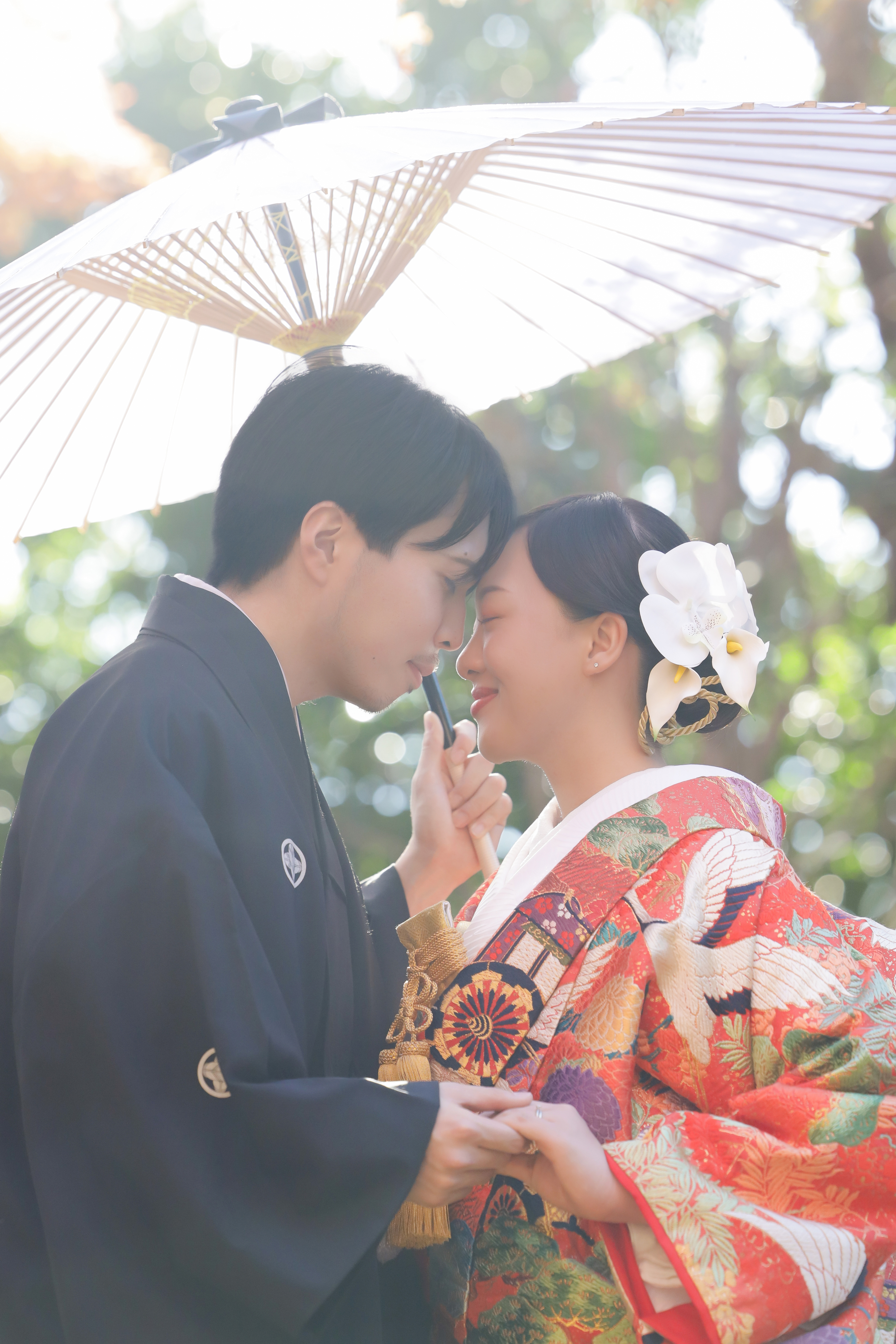 白い和傘の下で額を寄せ合う鶴文様の色打掛の新婦と黒紋付袴の新郎
