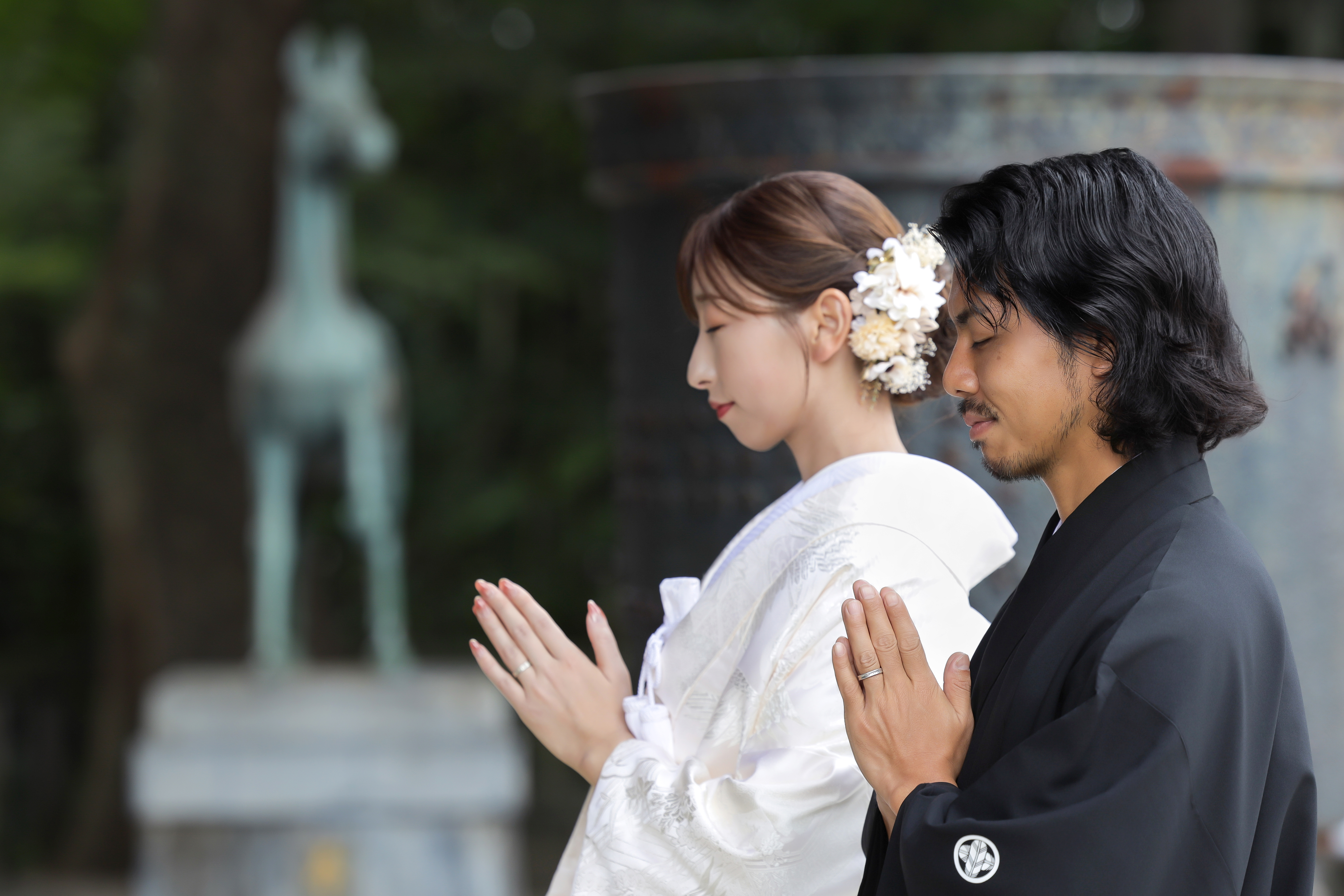 神社の境内で並んで手を合わせ祈る白無垢の新婦と黒紋付袴の新郎