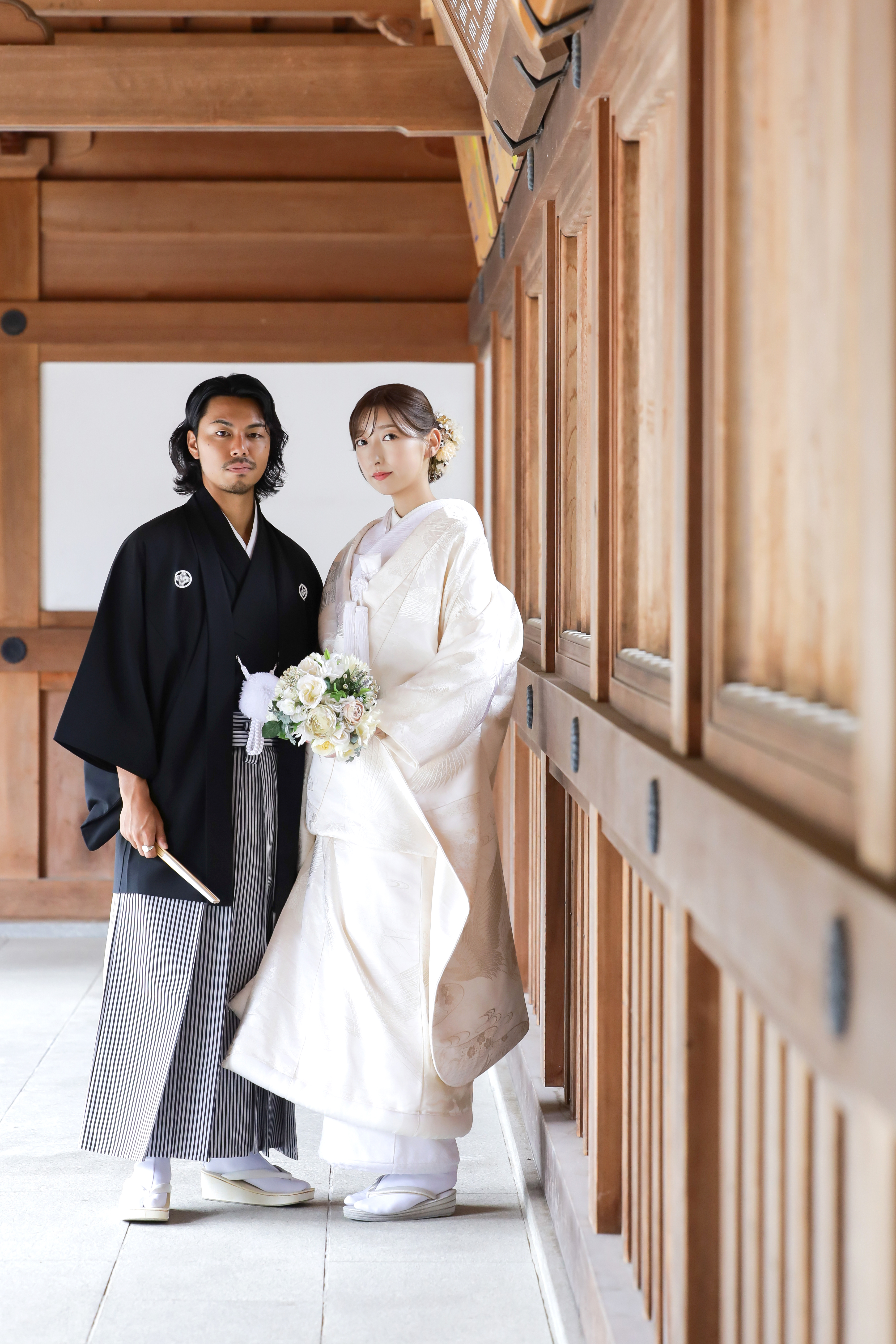 社殿の木造回廊でブーケを手にした白無垢の新婦と黒紋付袴の新郎