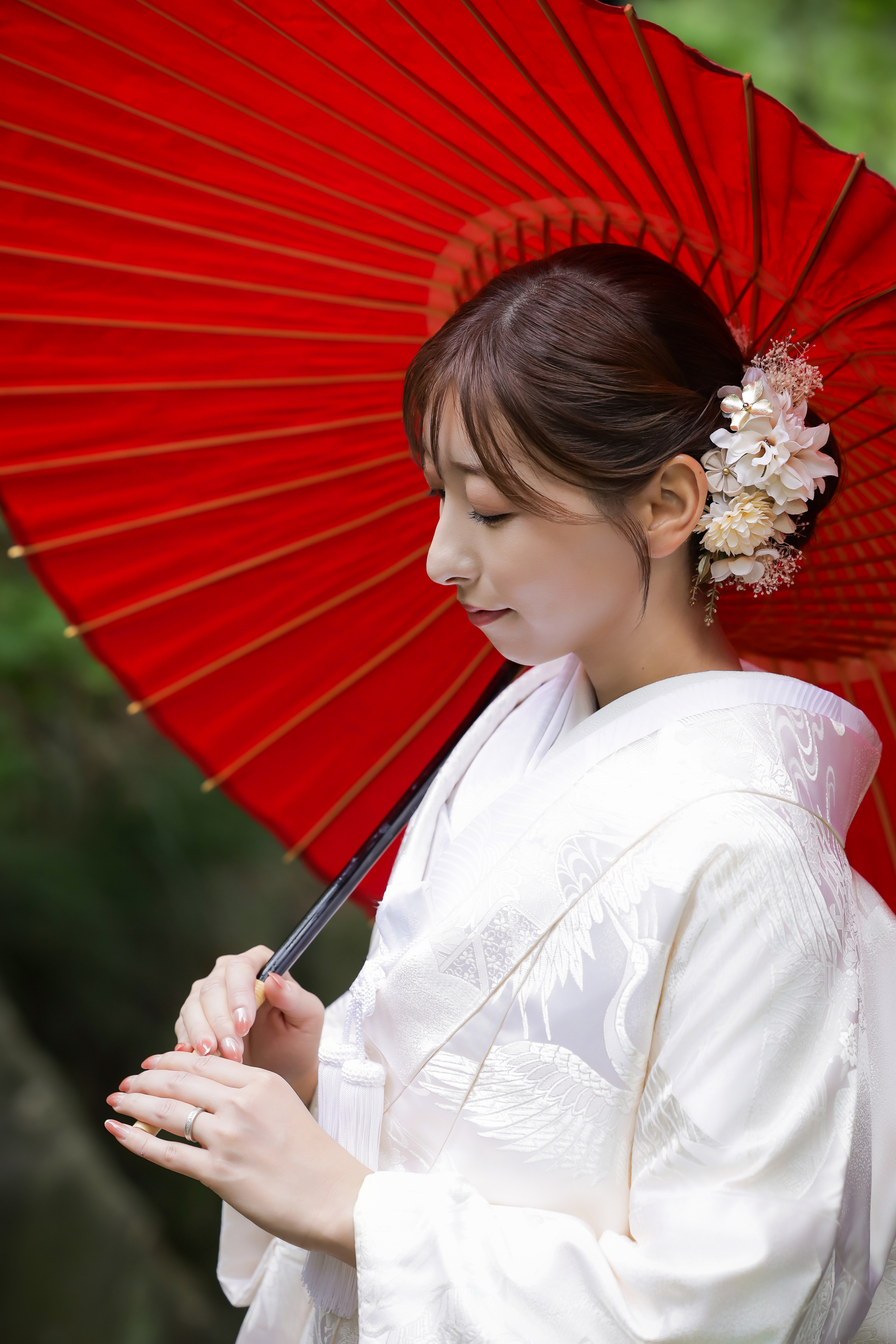 赤い和傘を手に目を伏せる鶴文様の白無垢姿の新婦の横顔