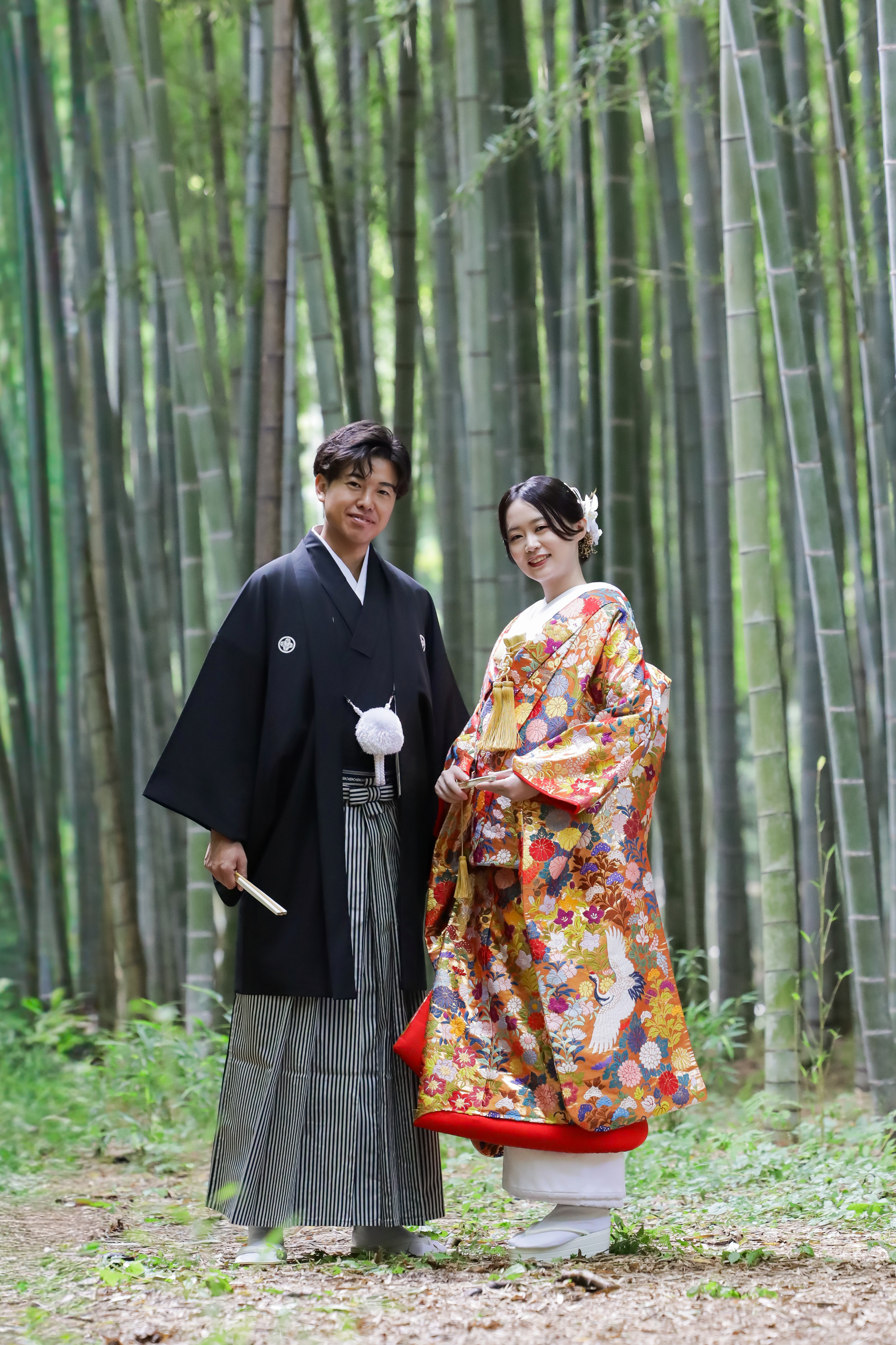 竹林を背にオレンジ地に鶴の色打掛をまとった新婦と黒紋付袴の新郎