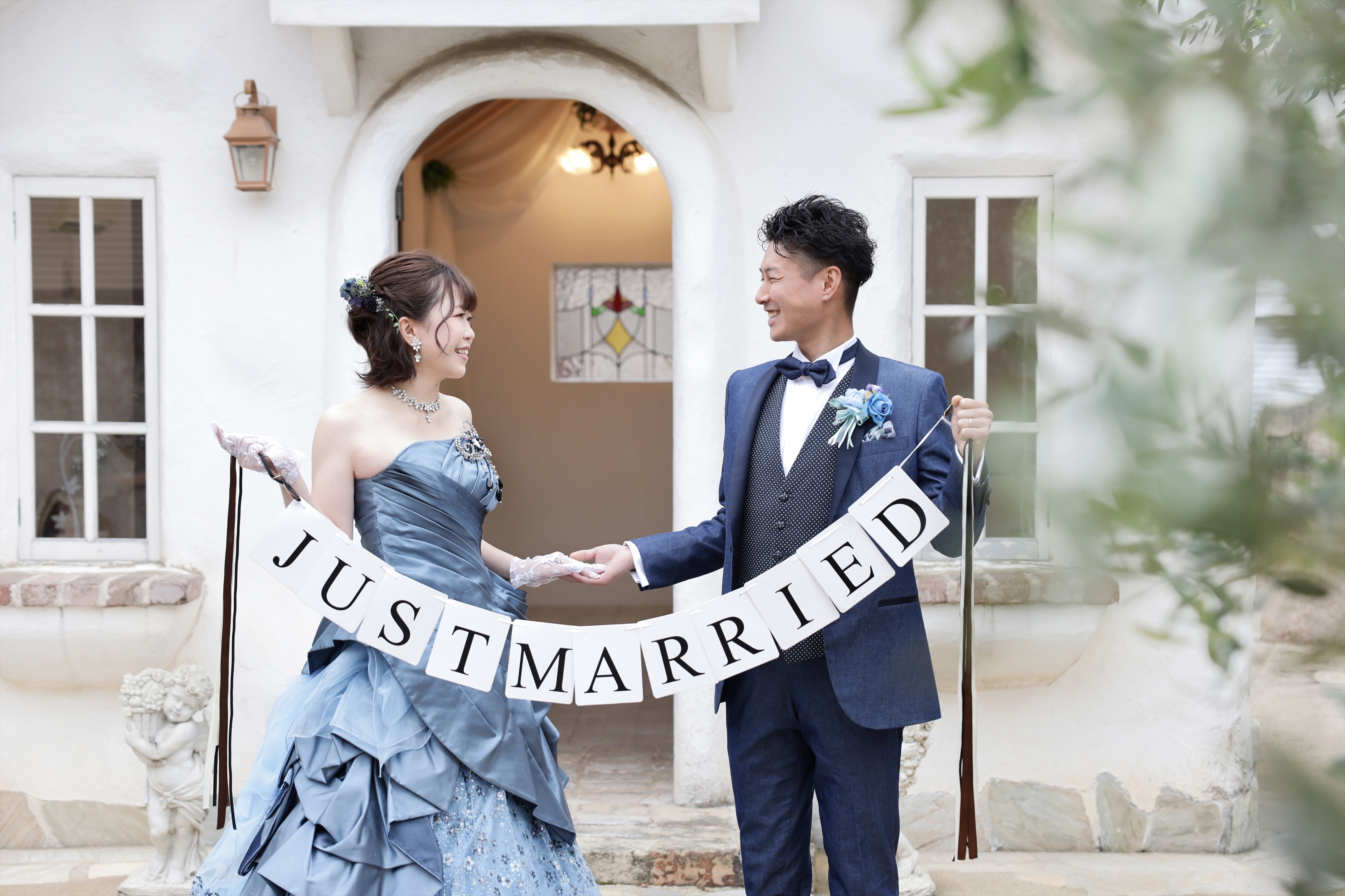 JUST MARRIEDのガーランドを持つブルーグレーのカラードレスとネイビータキシードの二人