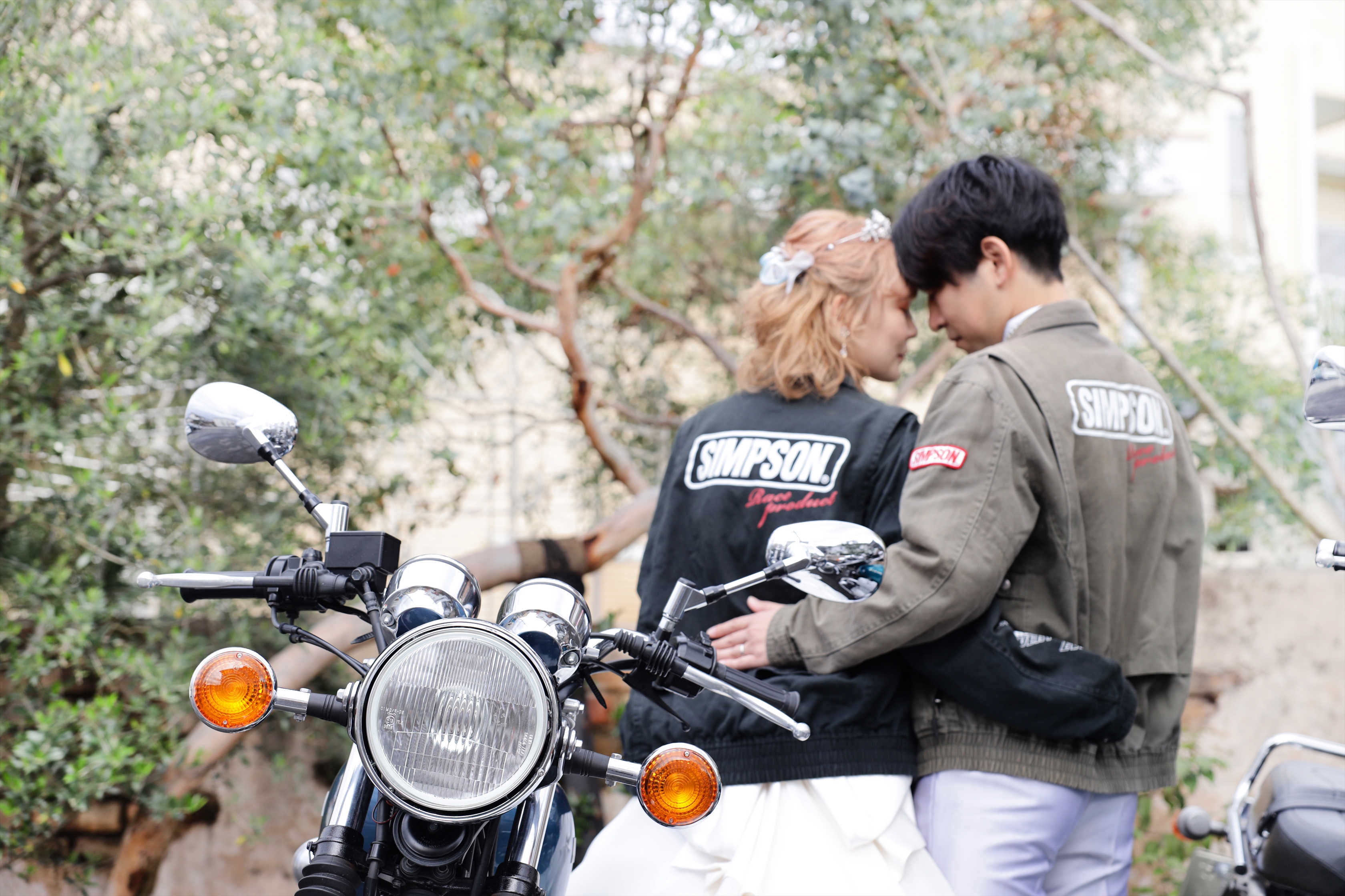 バイクの前でおそろいのレーシングジャケットを羽織り額を寄せ合う新郎新婦