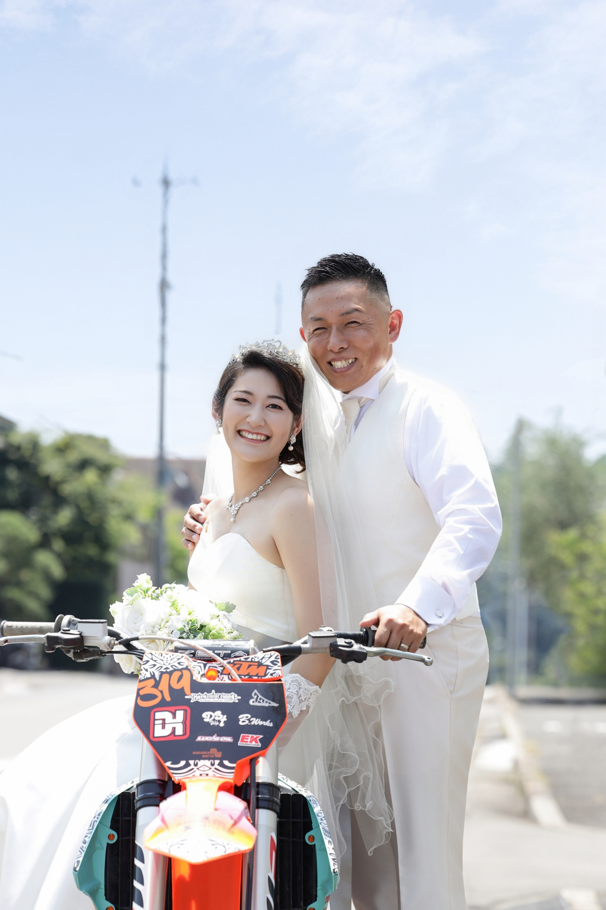 オフロードバイクにまたがりウェディングドレスと白タキシードで笑顔を見せる二人