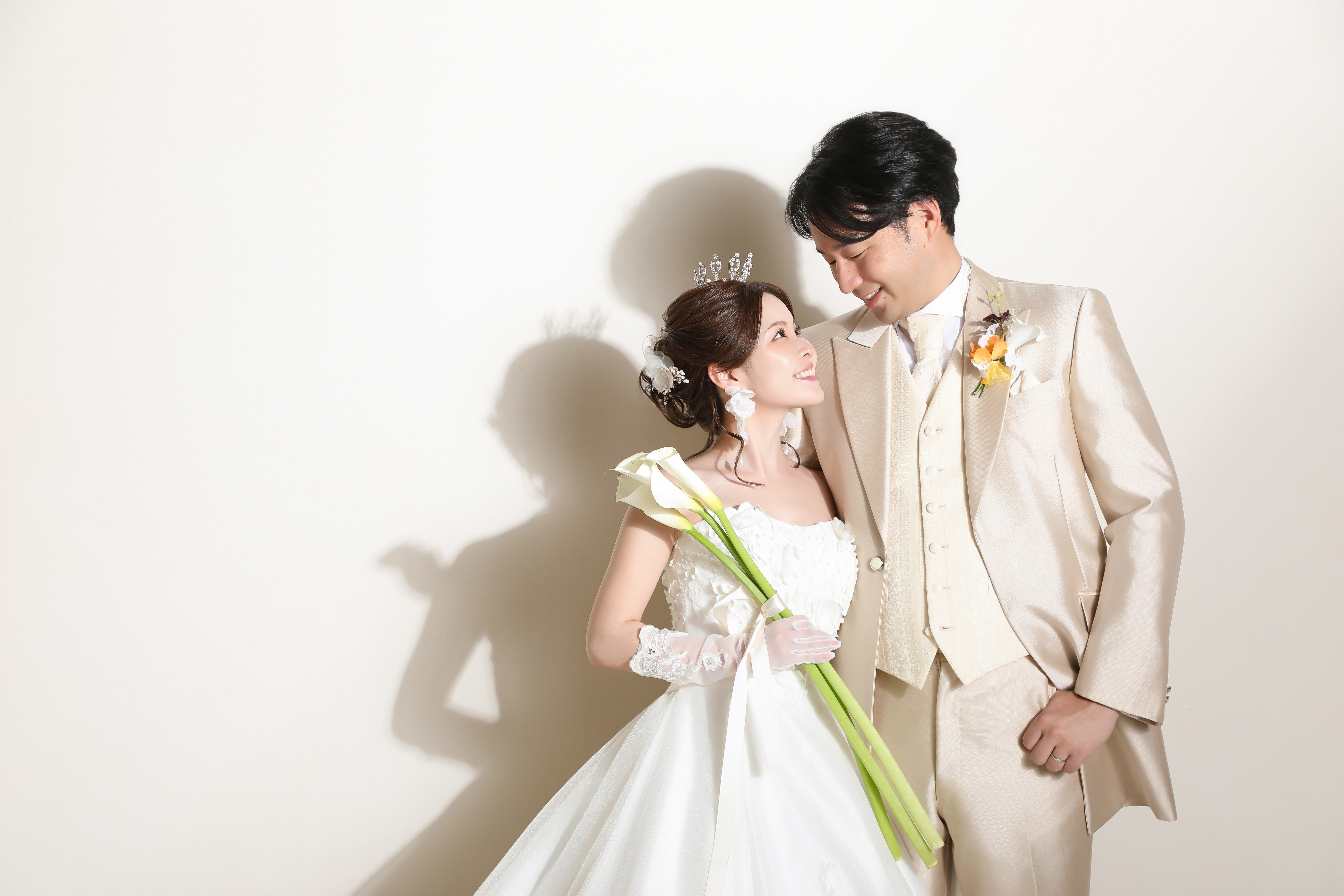 ティアラをつけたドレスの新婦を優しく見つめるベージュタキシードの新郎