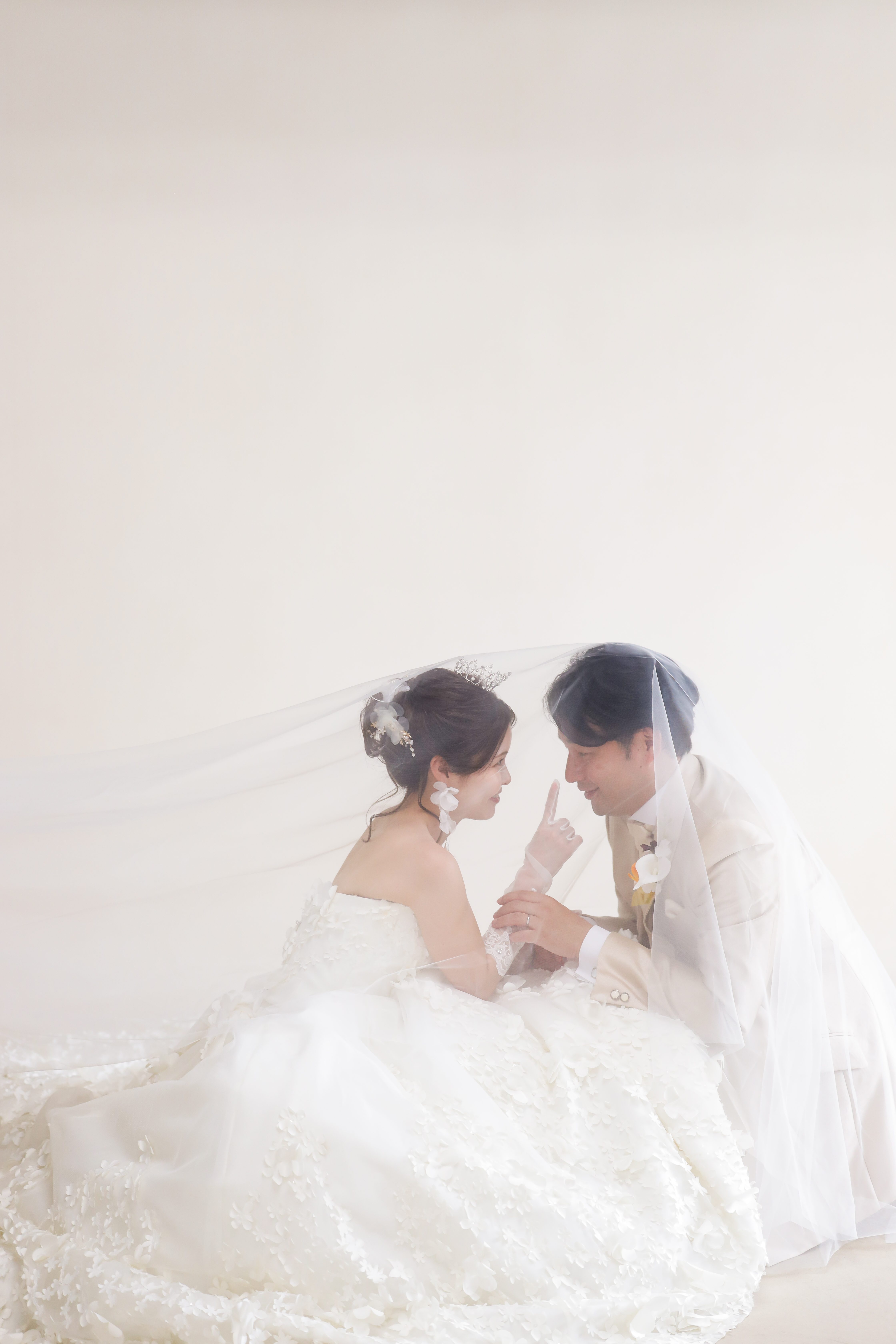 ふわりと広がるベールの中で顔を寄せ合うウェディングドレスの新婦と新郎