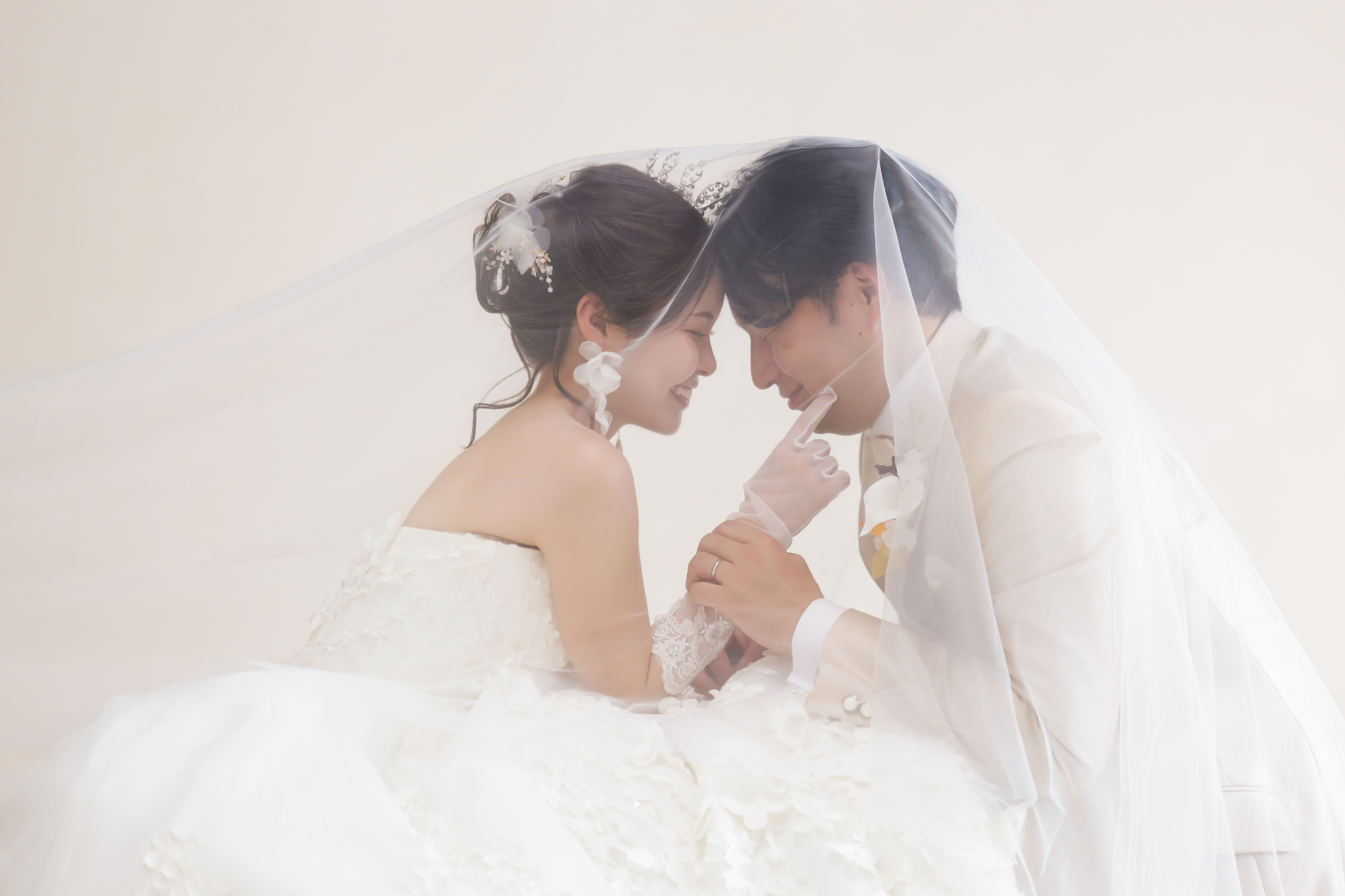 ベールに包まれ額を寄せて笑い合うウェディングドレスの新婦と新郎