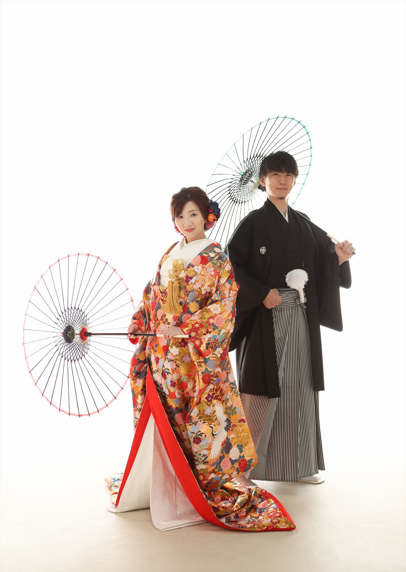 番傘を持ち白バックで背中合わせに立つ色打掛の花嫁と紋付袴の新郎