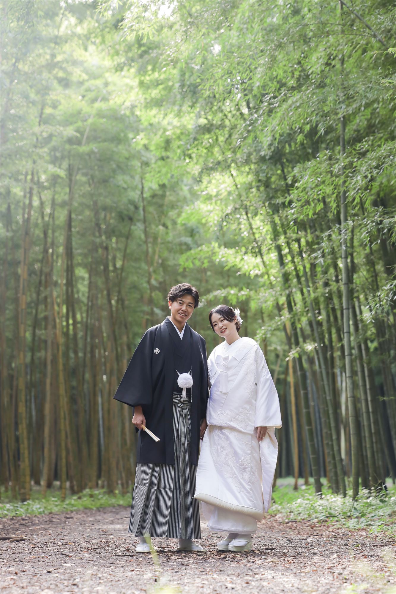 青々とした竹林の小径に寄り添って立つ白無垢の新婦と紋付袴の新郎