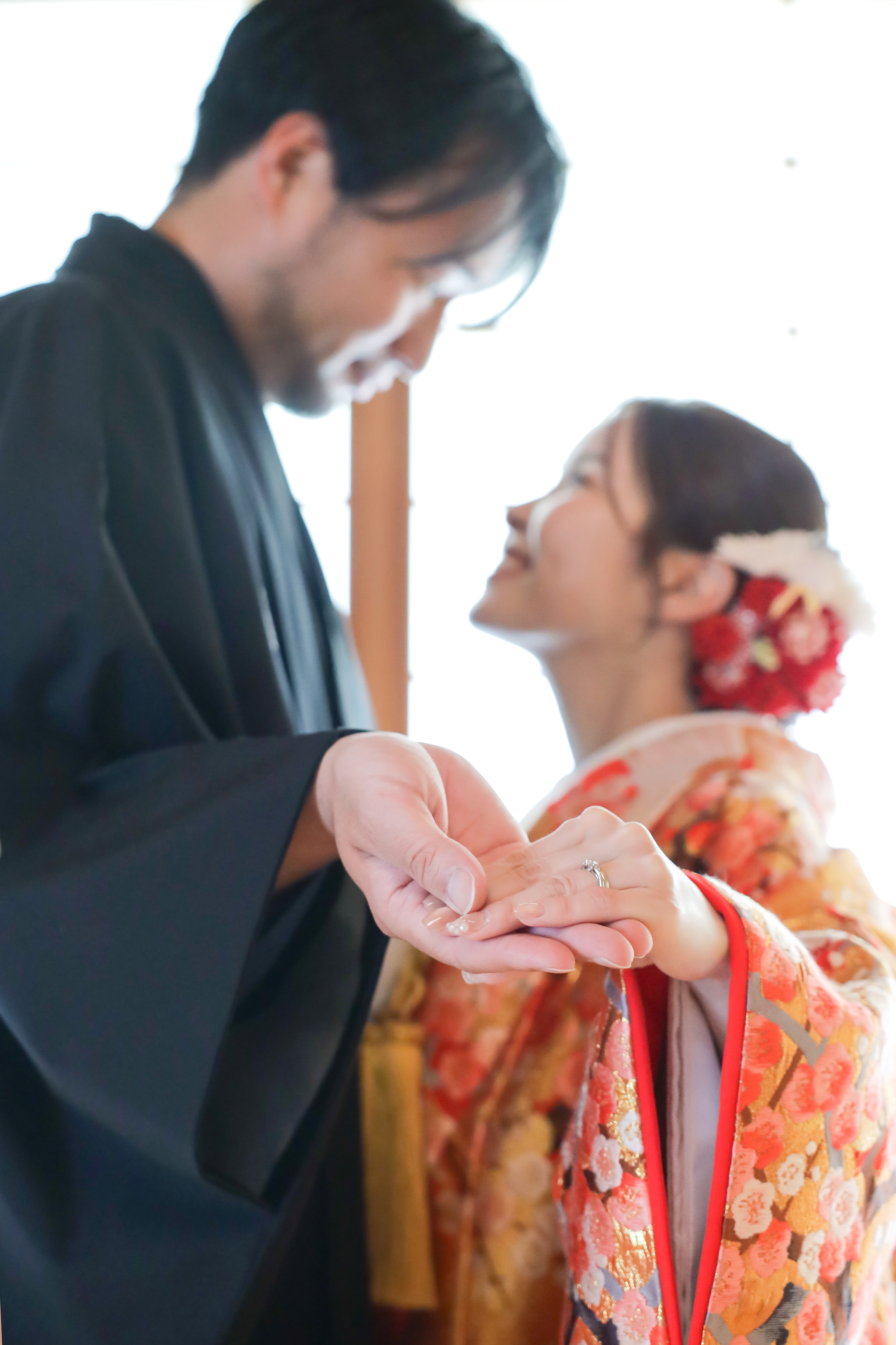 結婚指輪をつけた手を重ねる色打掛の新婦と黒紋付袴の新郎