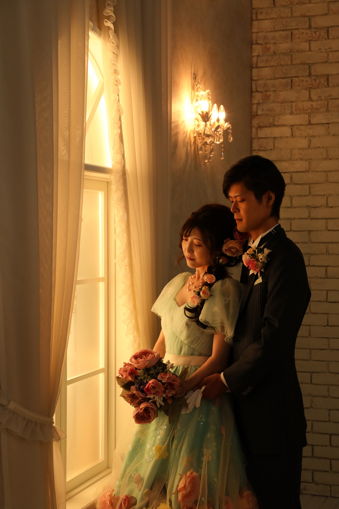 窓辺の灯りに照らされたミントグリーンのカラードレスの新婦と新郎