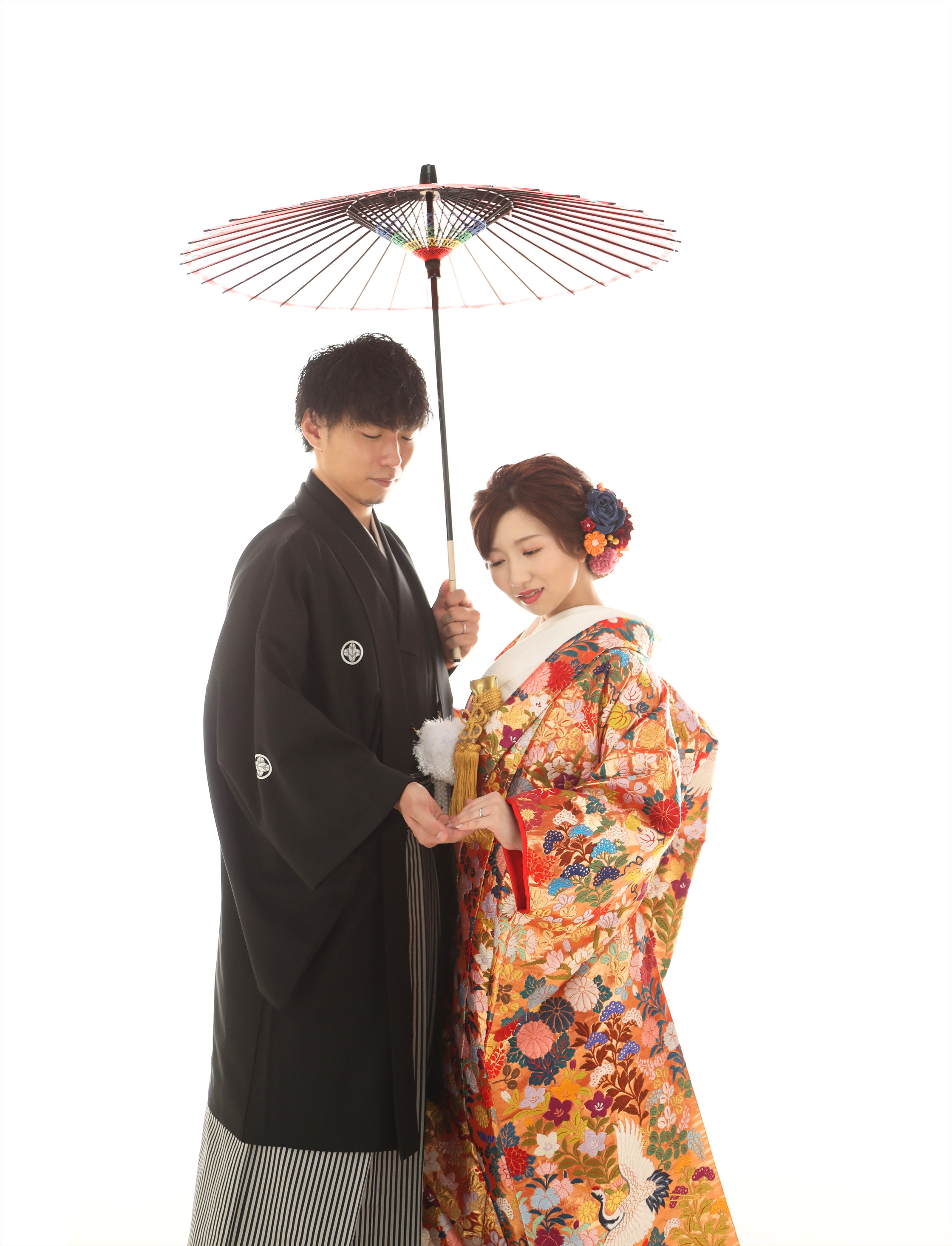 番傘をさす黒紋付袴の新郎とオレンジの色打掛をまとった新婦