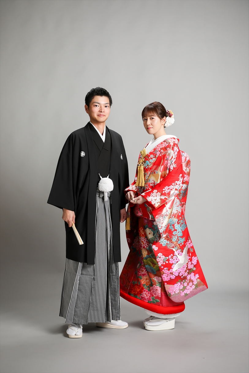 グレー背景のスタジオに並ぶ赤い色打掛の新婦と黒紋付袴の新郎