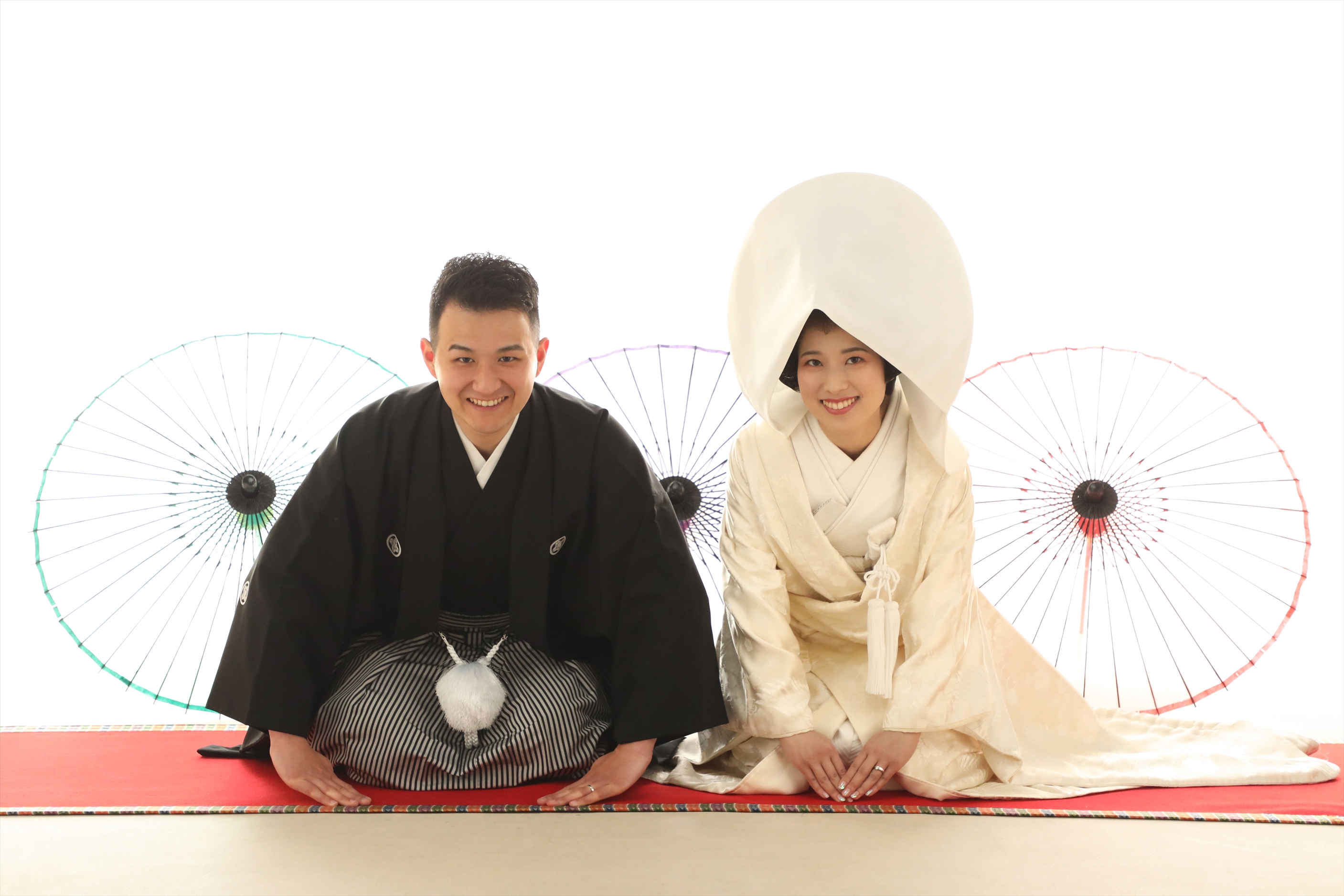 和傘を背に正座する白無垢に綿帽子の新婦と黒紋付袴の新郎