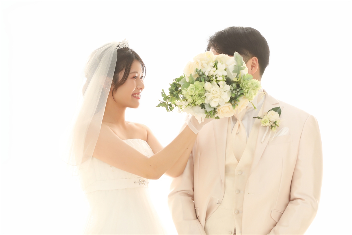 白い光に包まれたスタジオでブーケを差し出しほほえむウェディングドレスの新婦